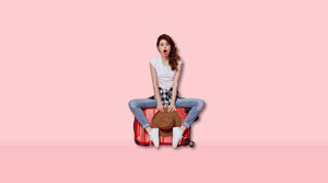 Woman sitting on a suitcase with a surprised face because she packed her magic wand discreetly with Quiver.love wand massager pouch